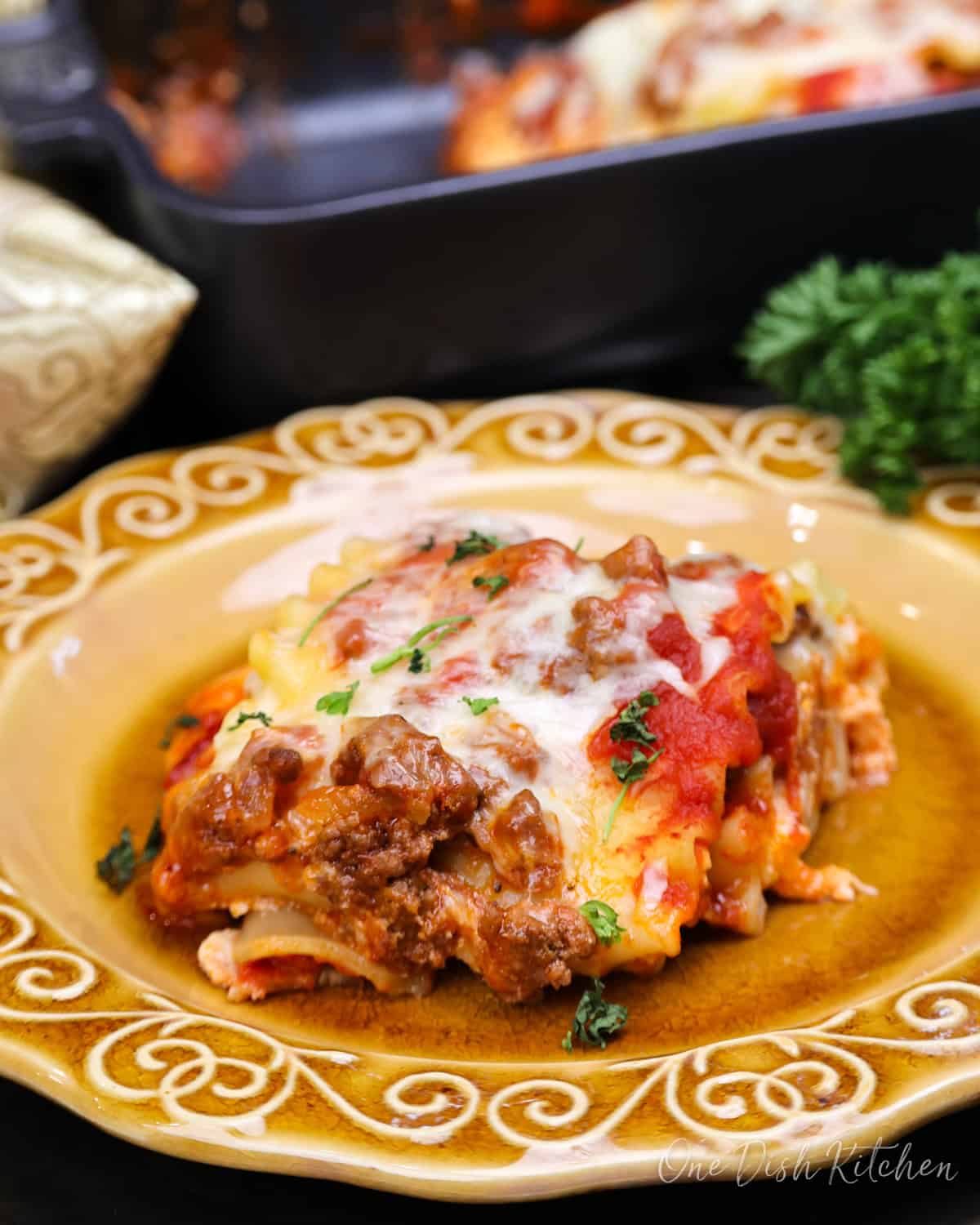 a single lasagna rollup on a plate next to a baking dish filled with a small batch of lasagna rollups.
