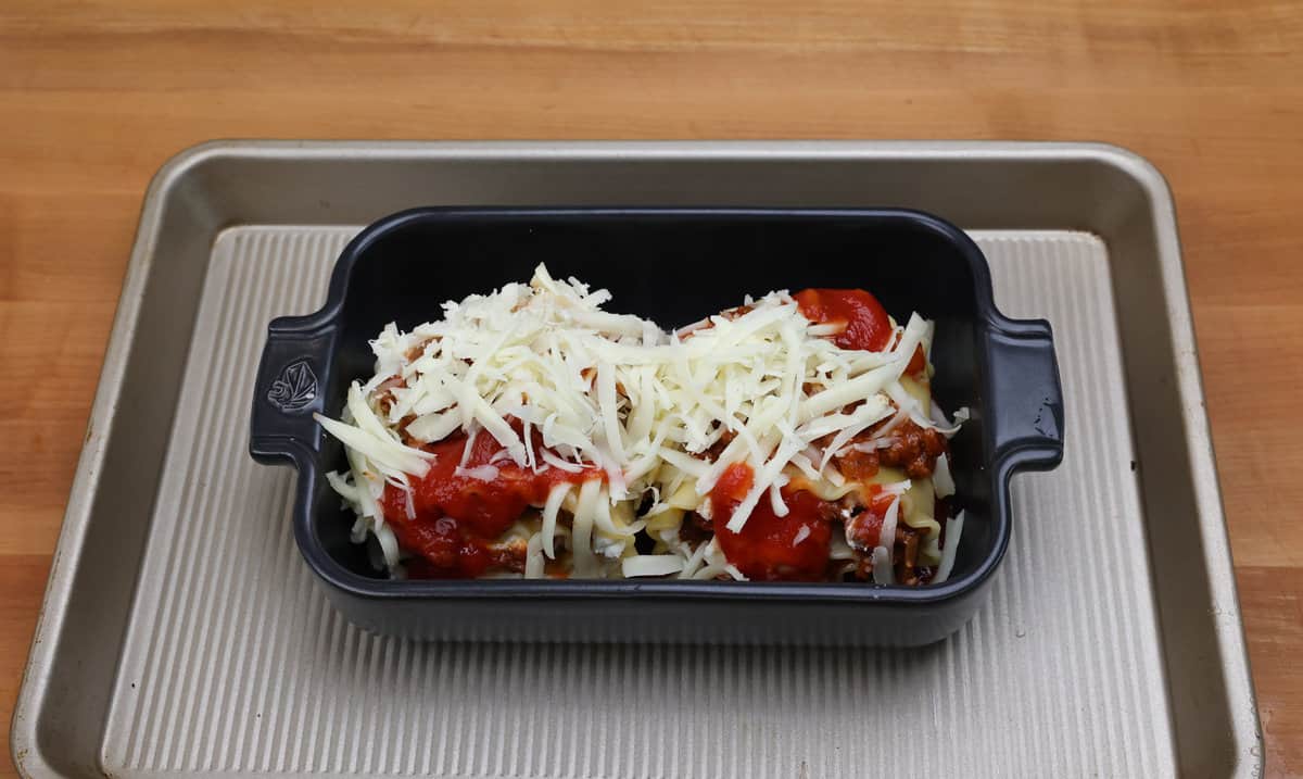 two unbaked lasagna rolls in a baking dish topped with shredded mozzarella cheese.