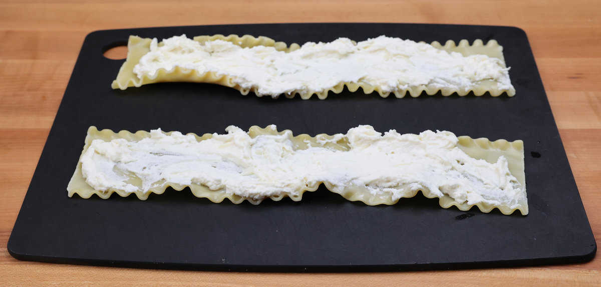 ricotta cheese spread across two lasagna noodles on a cutting board.