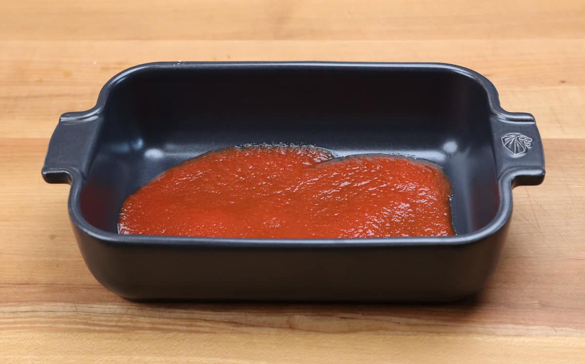 tomato sauce spread across the bottom of a small baking dish.
