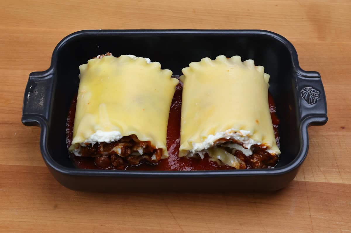 two stuffed lasagna noodles rolled in a baking dish.