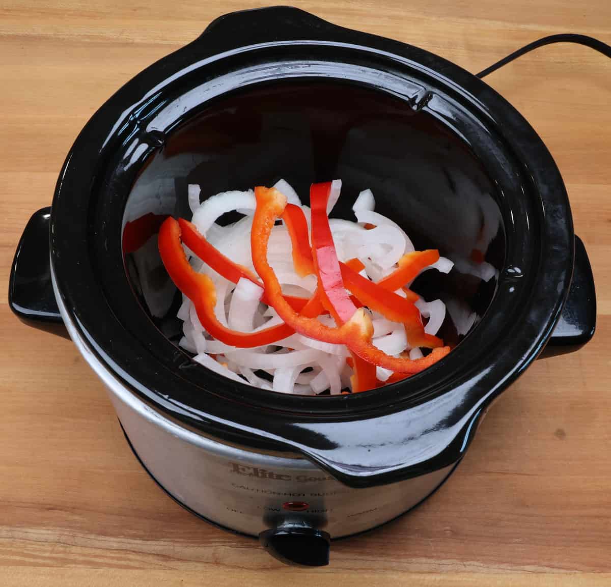 sliced onions and red bell peppers in the base of a slow cooker.