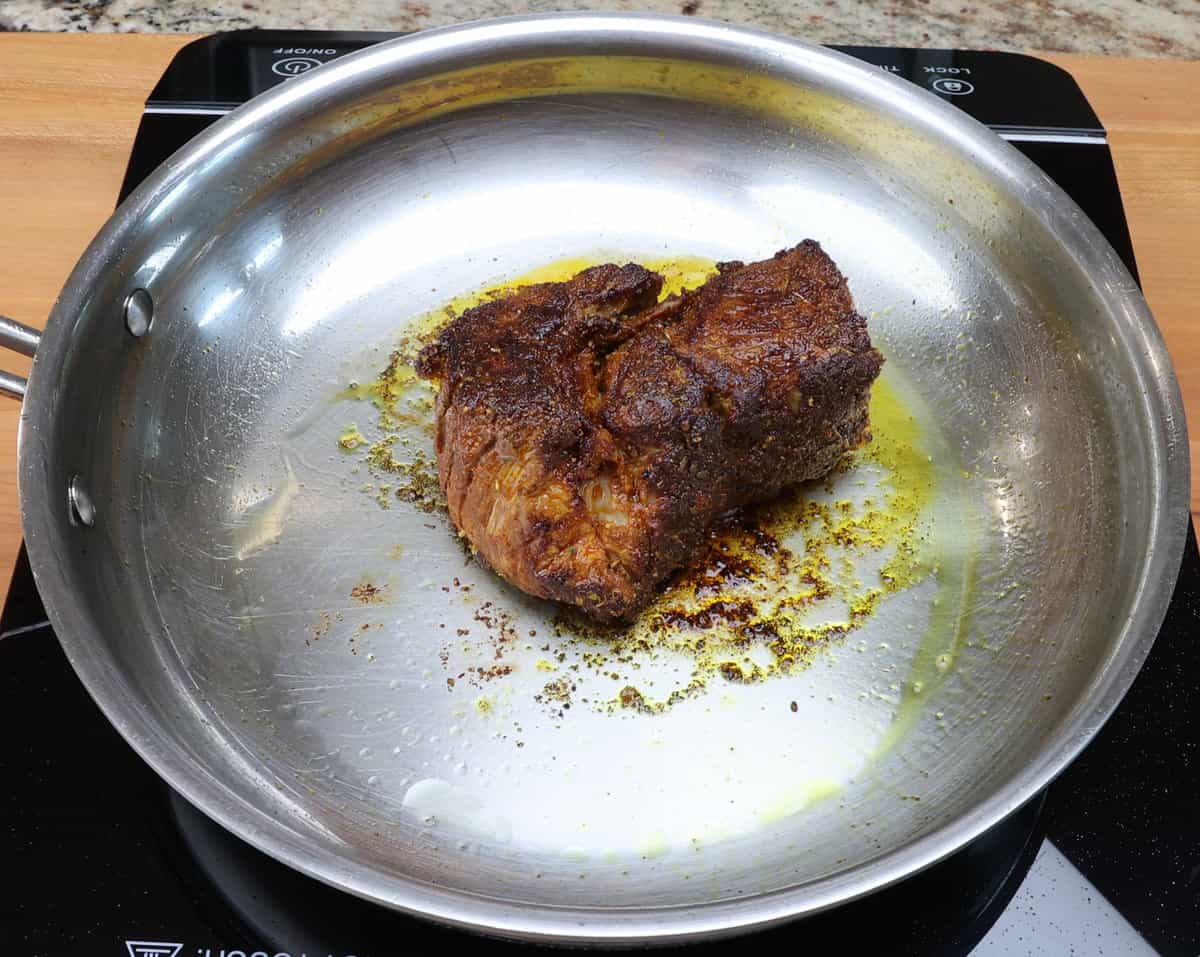 chuck roast being seared in a skillet on the stove.