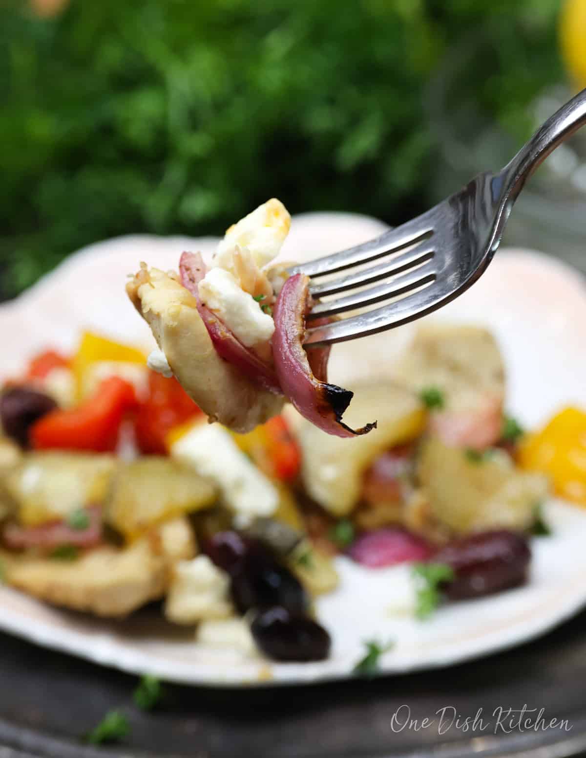 a fork filled with chicken and onions above a plate of vegetables.