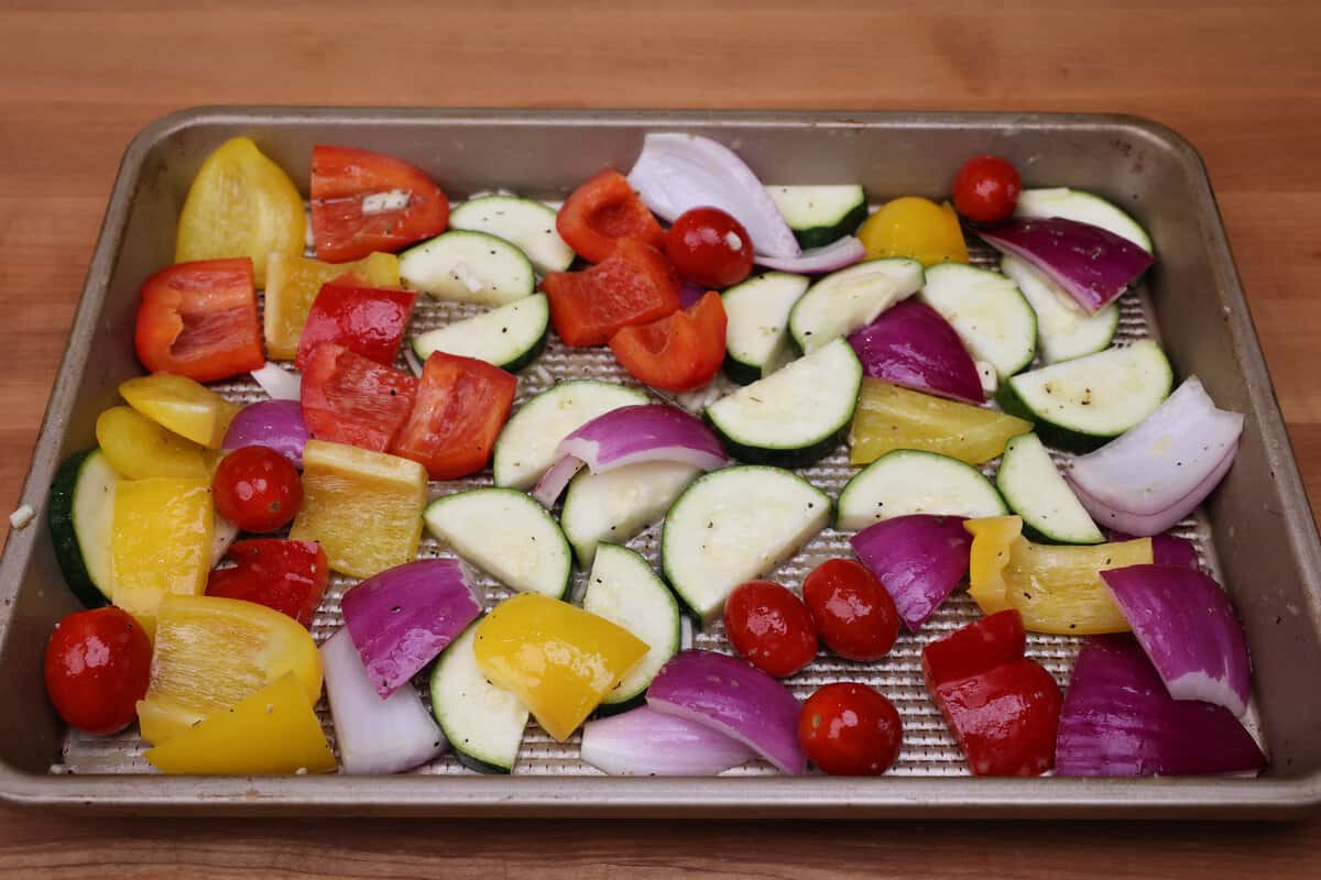 vegetables on a sheet pan tossed with oil and herbs.