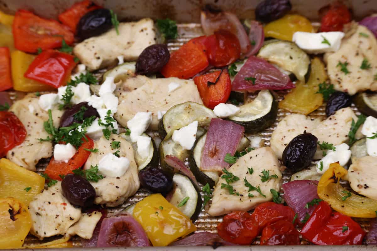 onions, peppers, chicken, feta, and olives on a sheet pan.