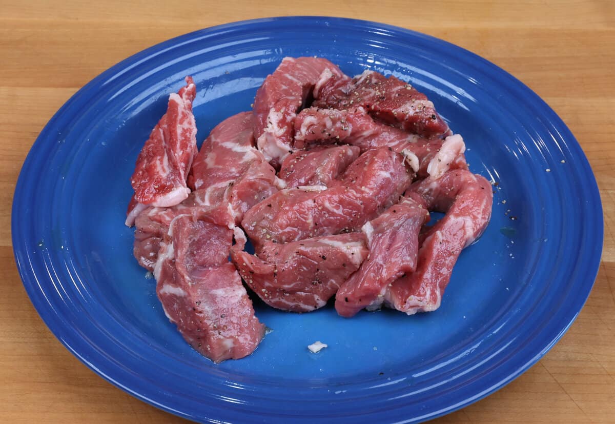 raw slices of steak on a plate tossed with salt and pepper.