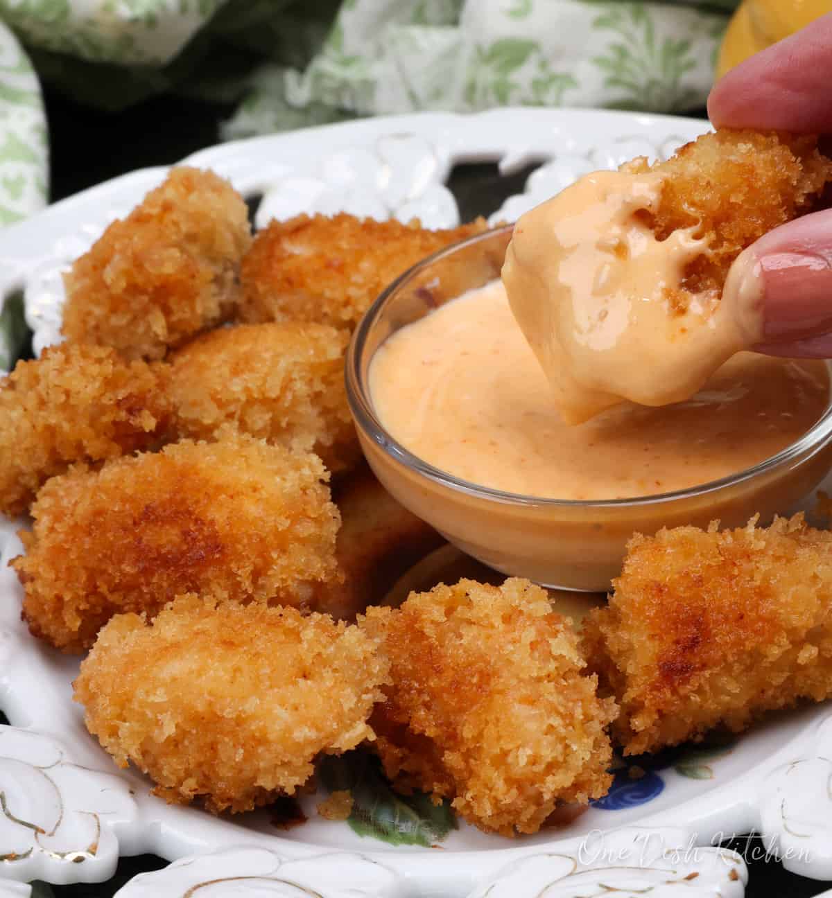 a chicken nugget in dipping sauce next to a plate with other chicken nuggets.