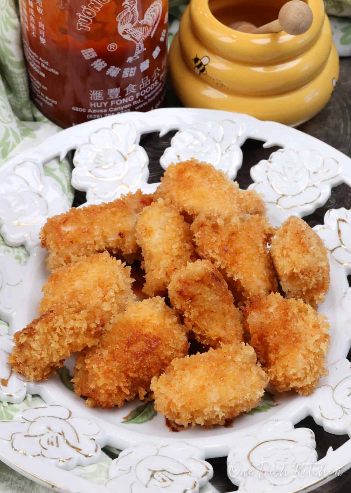 a plate of chicken nuggets next to a jar of honey and a bottle of sriracha.