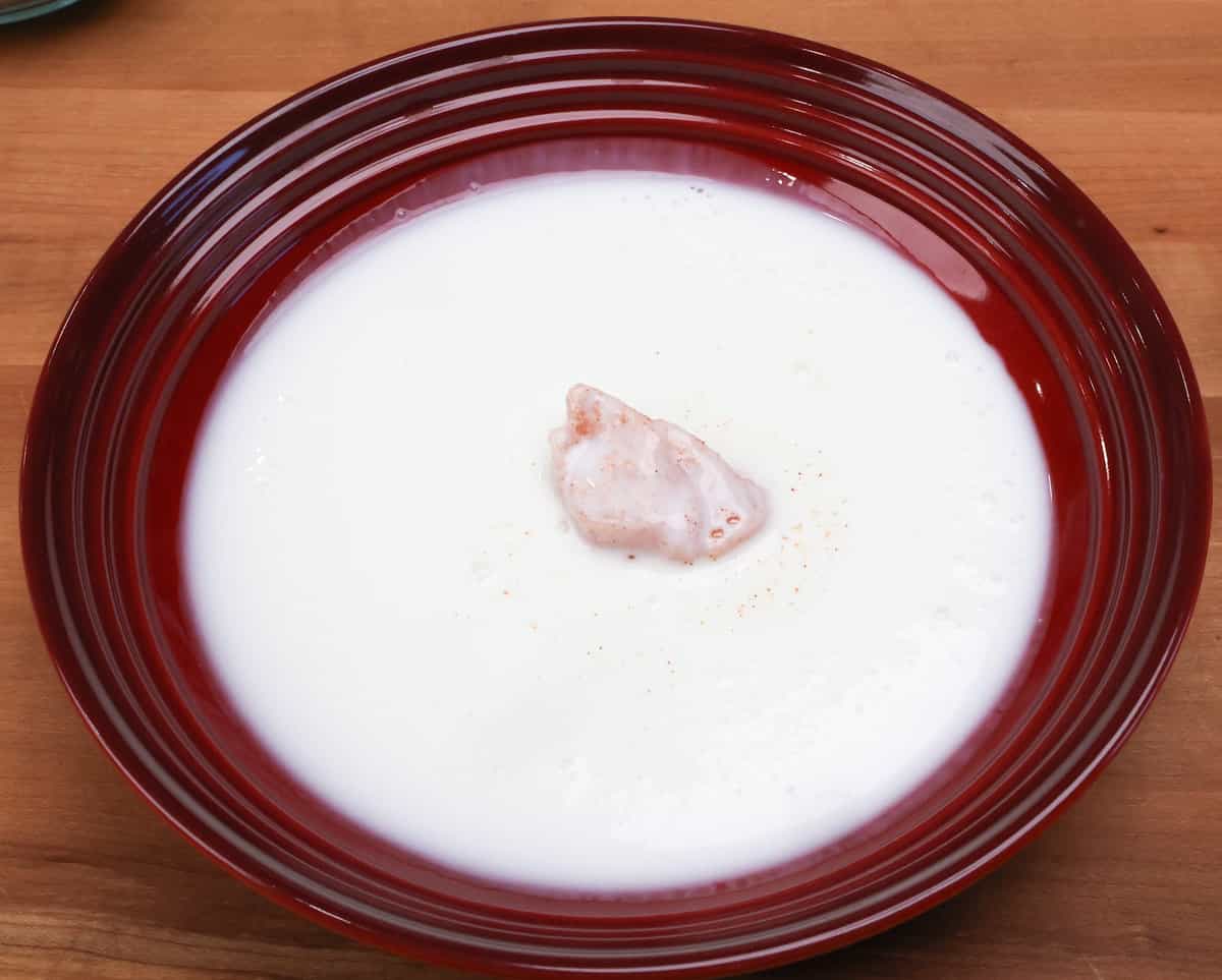 a floured piece of chicken in a bowl of buttermilk.