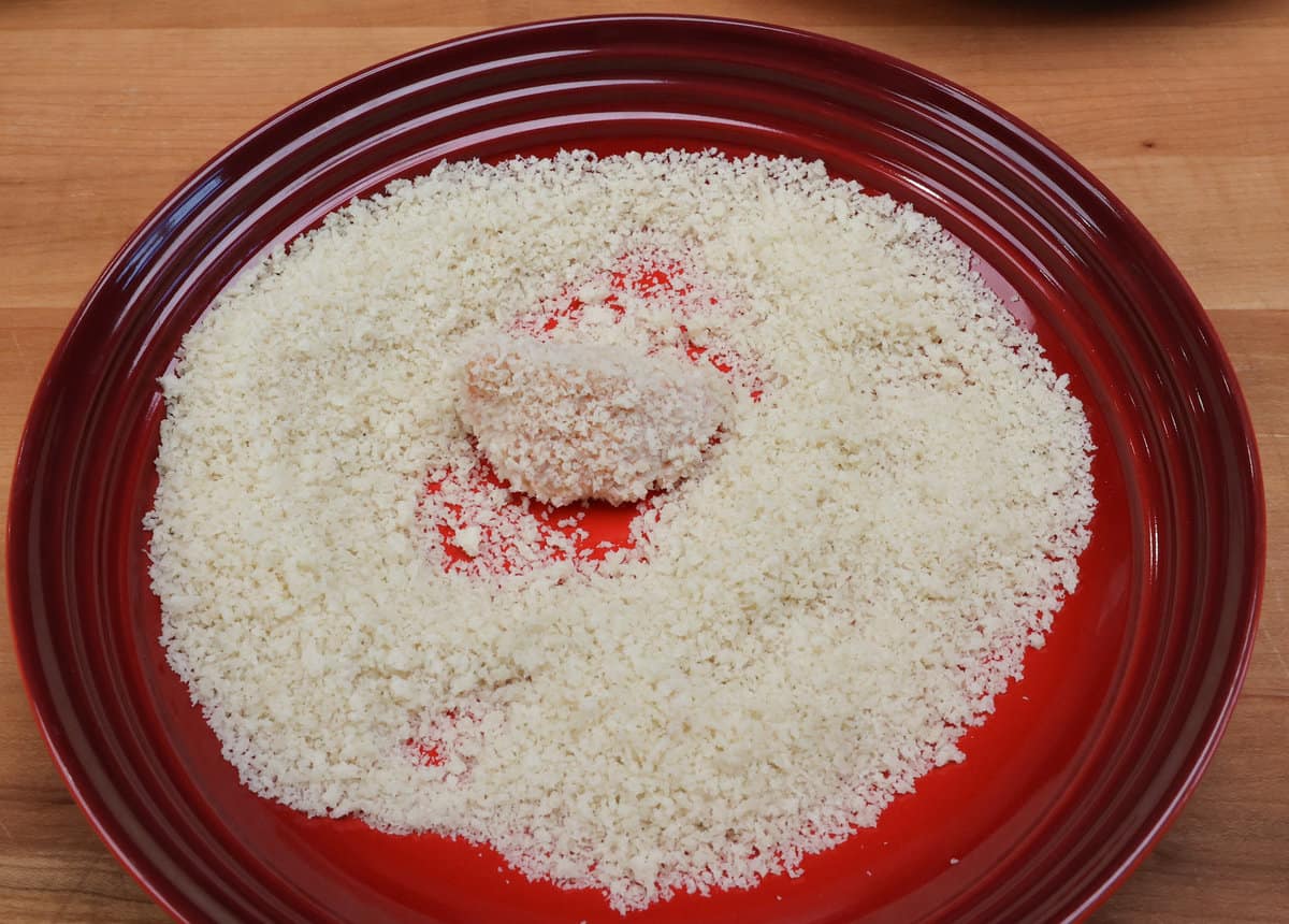 a chicken nugget dredged in breadcrumbs in a red bowl.