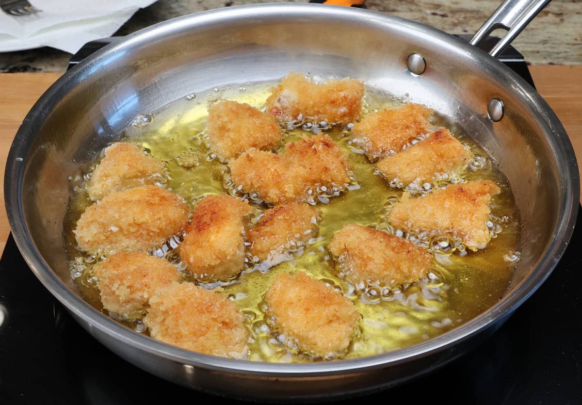 chicken nuggets frying in a skillet on the stove.