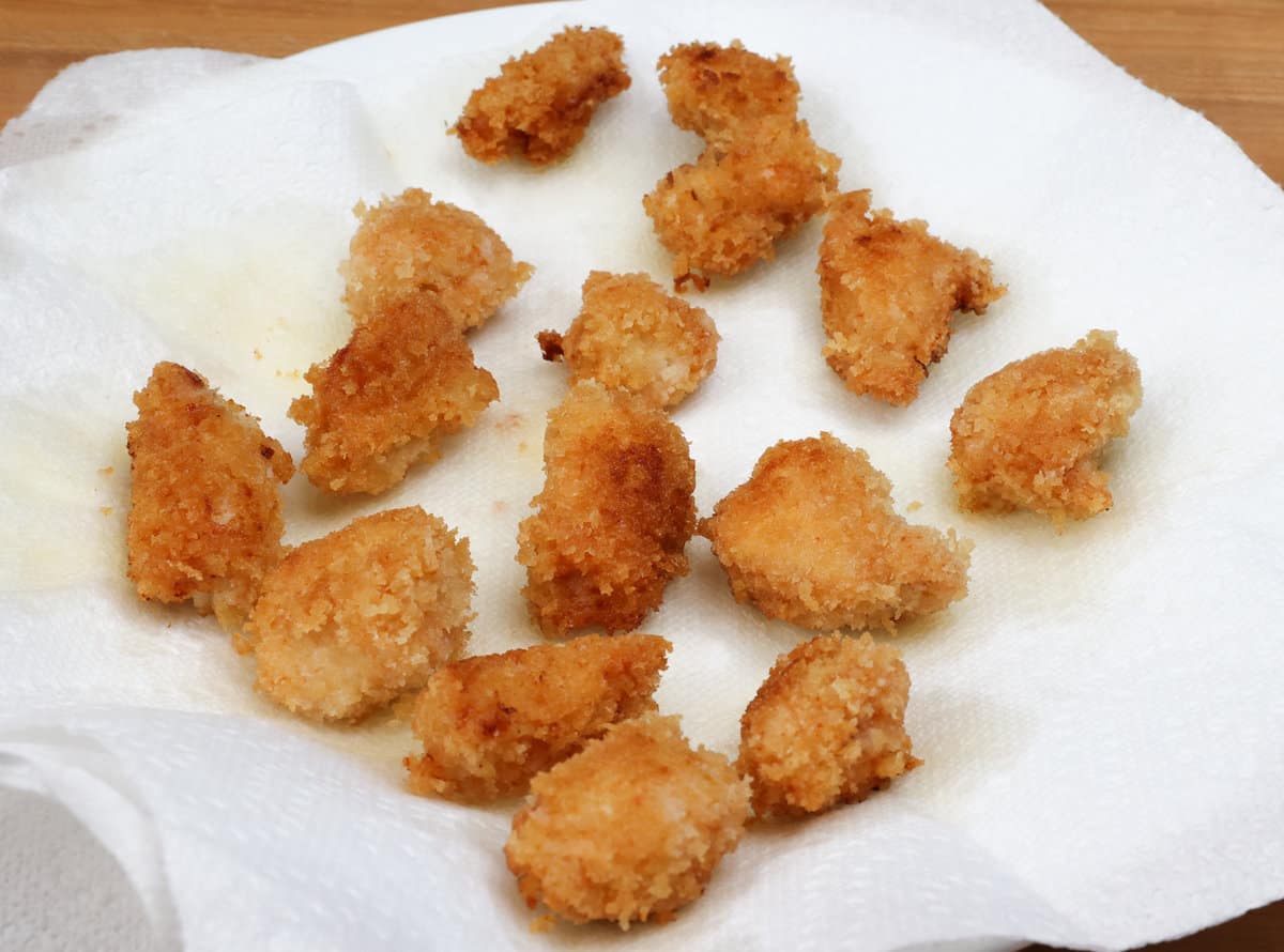 fried chicken nuggets draining on a paper towel-lined plate.
