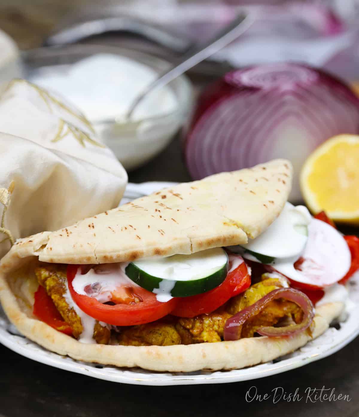 chicken shawarma in a pita topped with tomatoes, cucumbers, and red onions. 