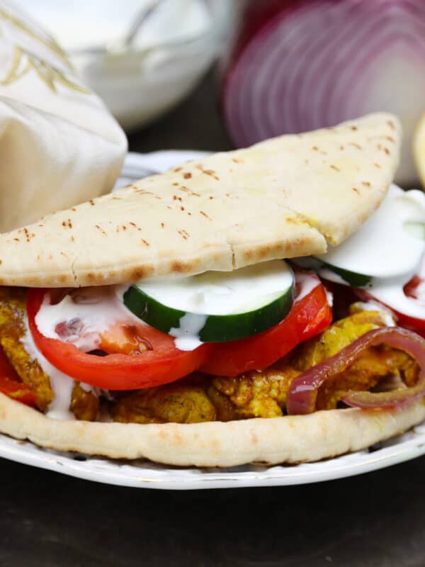 chicken shawarma in a pita topped with tomatoes, cucumbers, and red onions.
