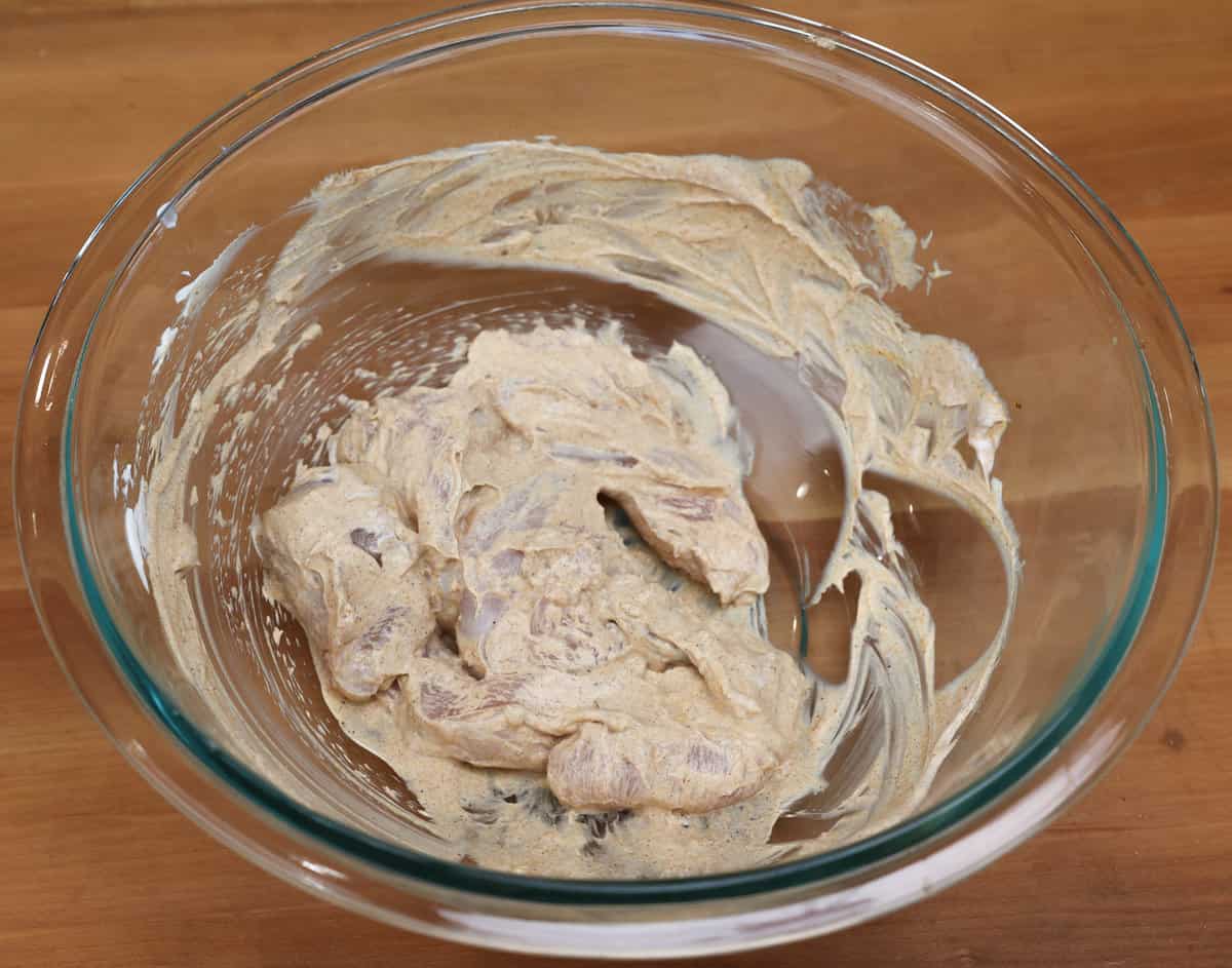 chicken pieces marinating in a yogurt sauce in a bowl.