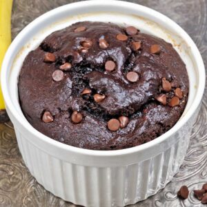 a small chocolate banana bread topped with chocolate chips in a white ramekin.