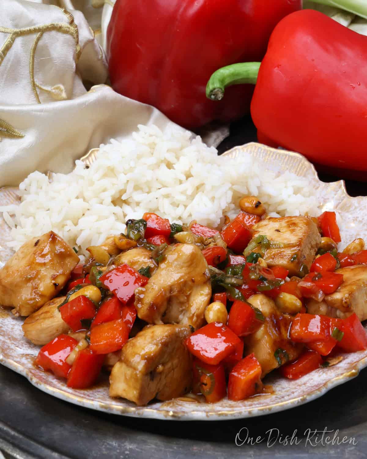 kung pao chicken on a white plate next to white rice on a silver tray.