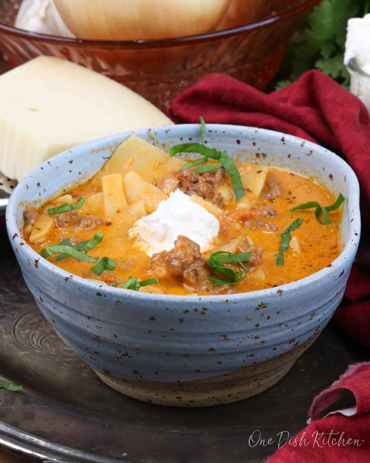 a blue bowl filled with lasagna soup topped with ricotta cheese and fresh basil.