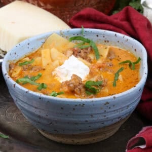 a blue bowl filled with lasagna soup topped with ricotta cheese and fresh basil.
