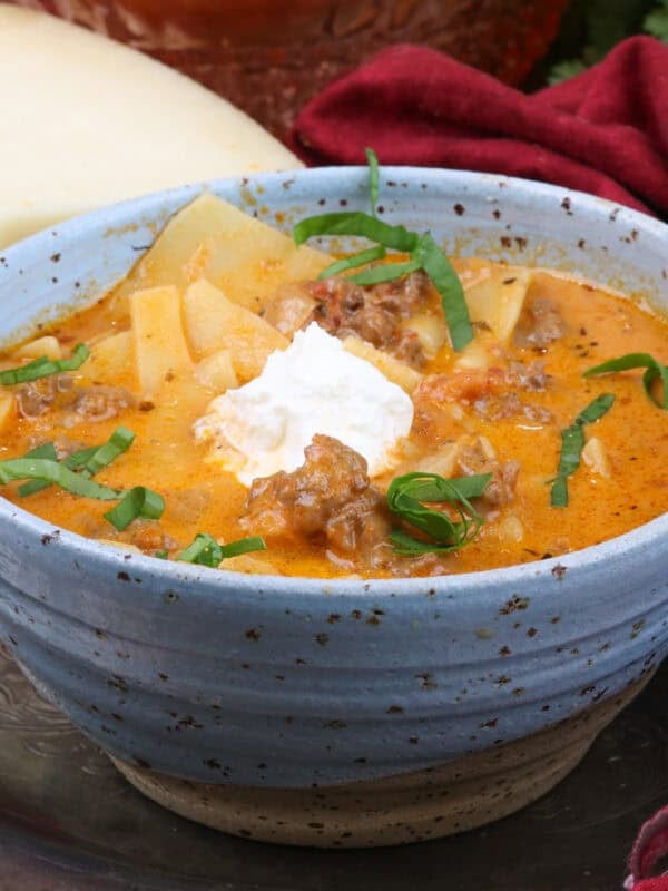 a blue bowl filled with lasagna soup topped with ricotta cheese and fresh basil.
