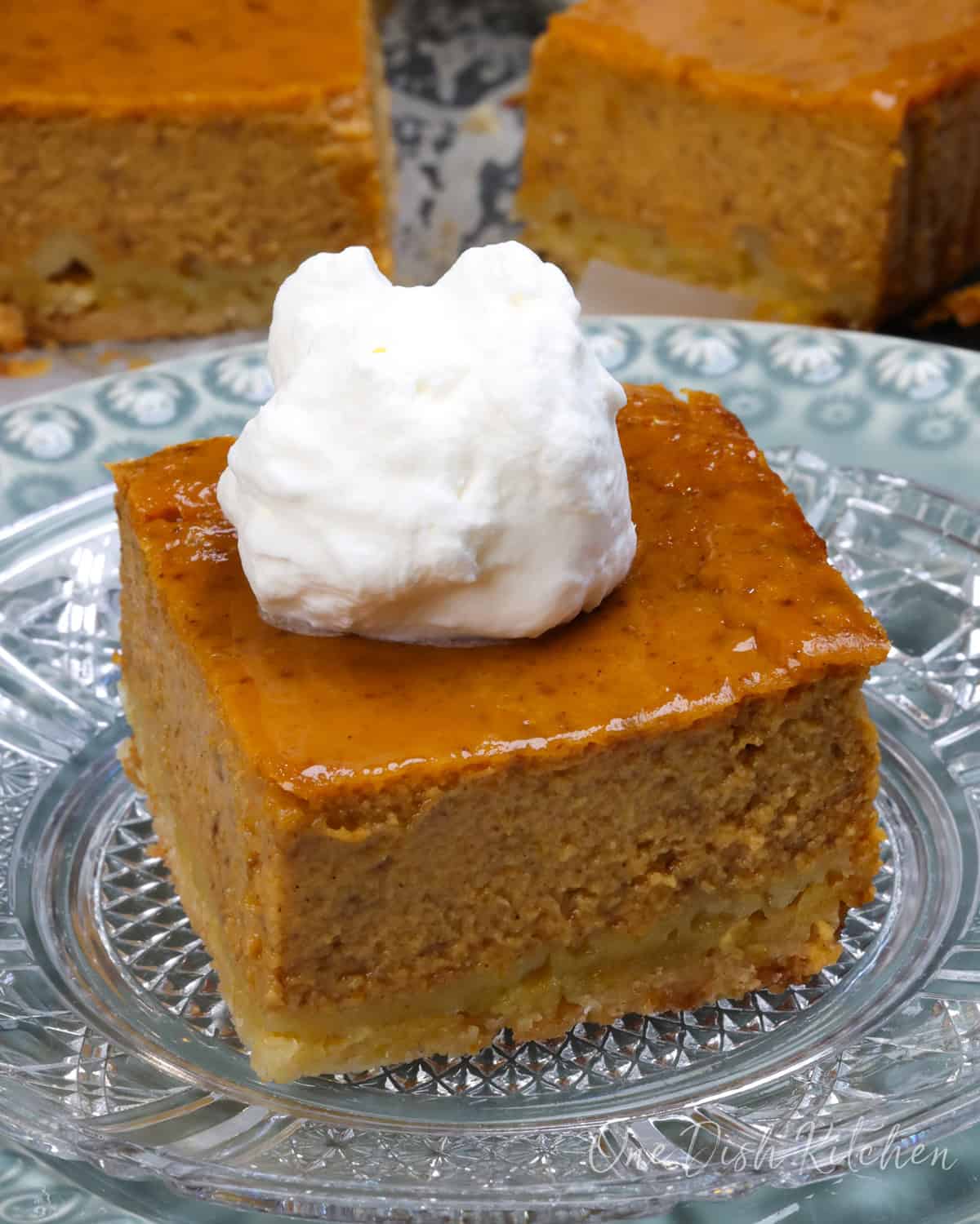 a pumpkin pie bar topped with whipped cream on a plate next to three pumpkin pie bars and a jar or whipped cream.