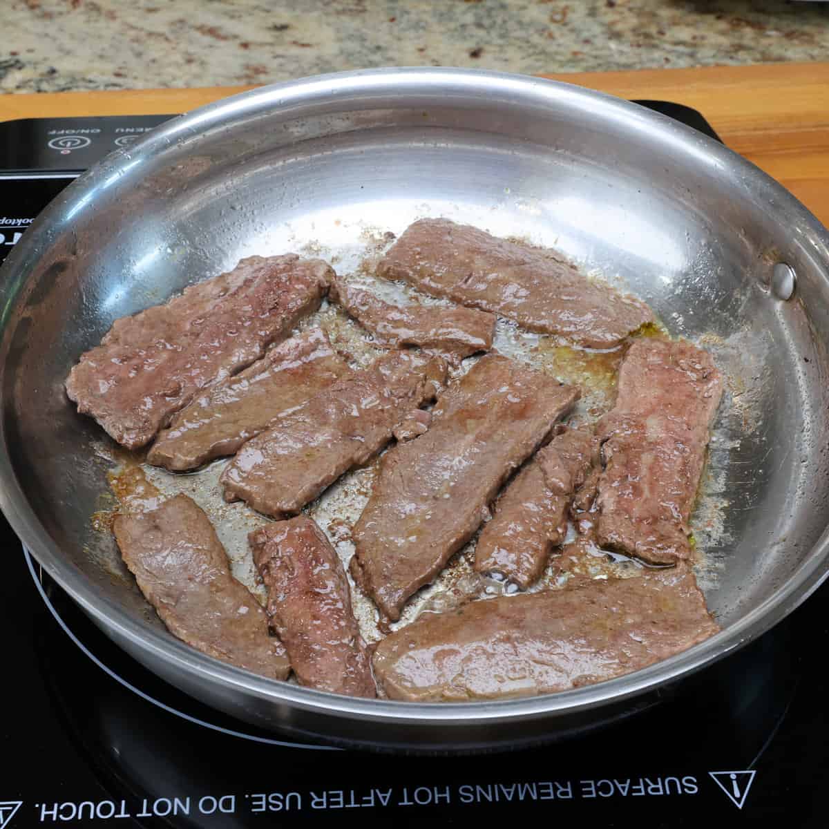 strips of beef cooking in a skillet.