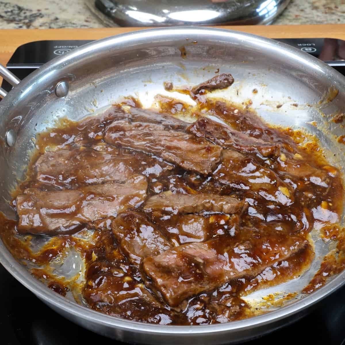 beef cooking in stir fry sauce in a skillet.