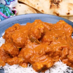 chicken tikka masala over white rice on a blue plate next to a plate of naan.