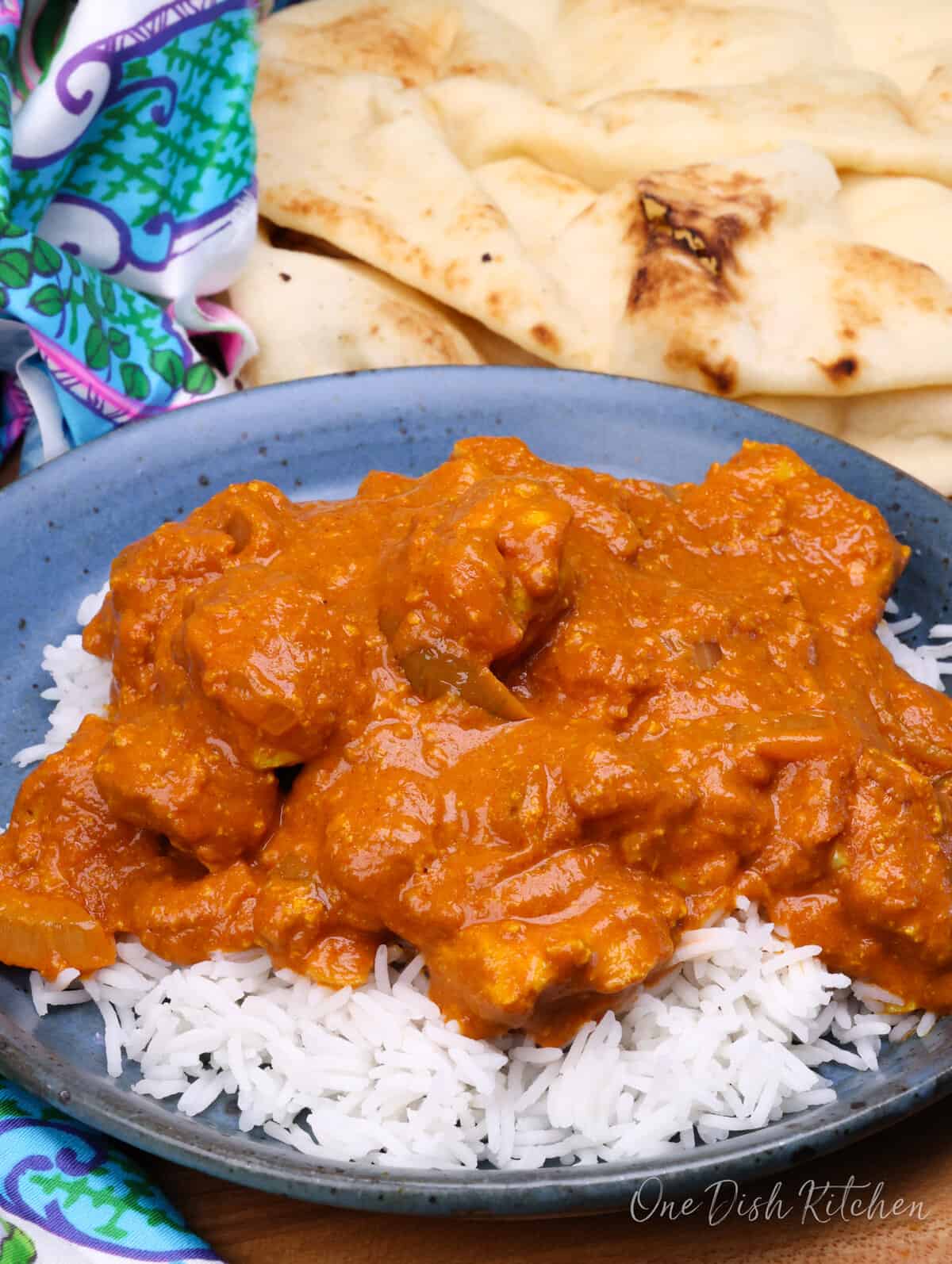 chicken tikka masala over white rice on a blue plate next to a plate of naan.