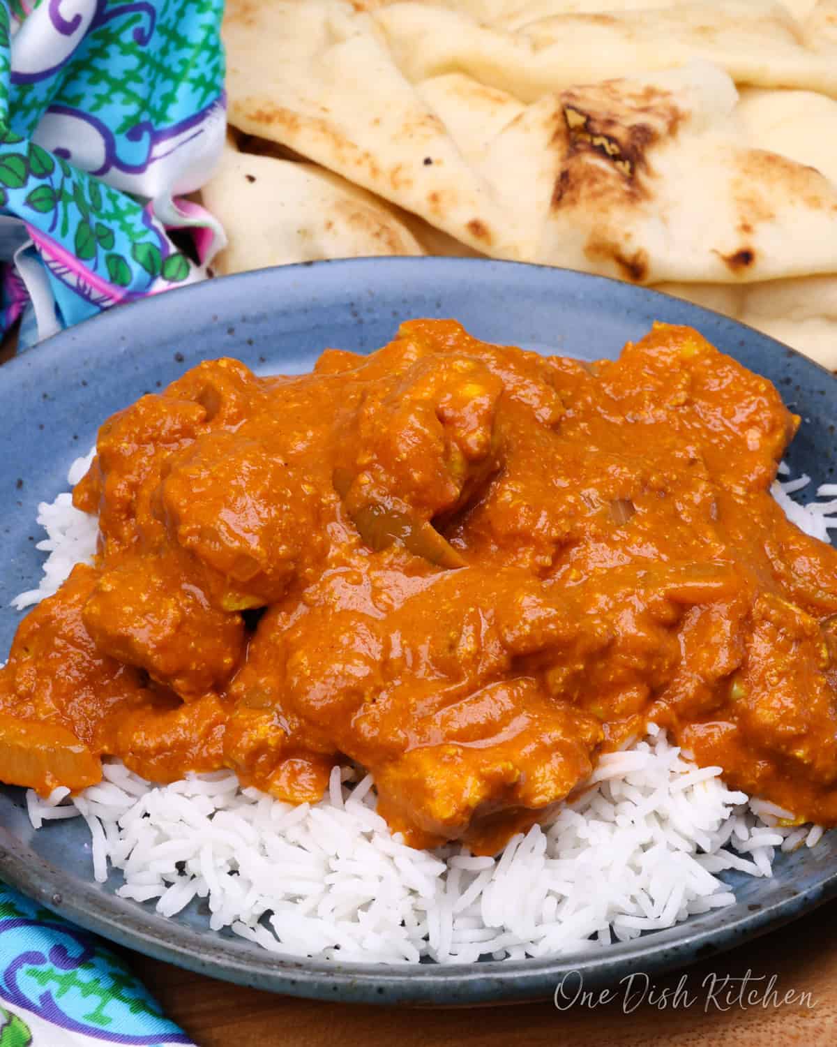chicken tikka masala over white rice on a blue plate next to a plate of naan.
