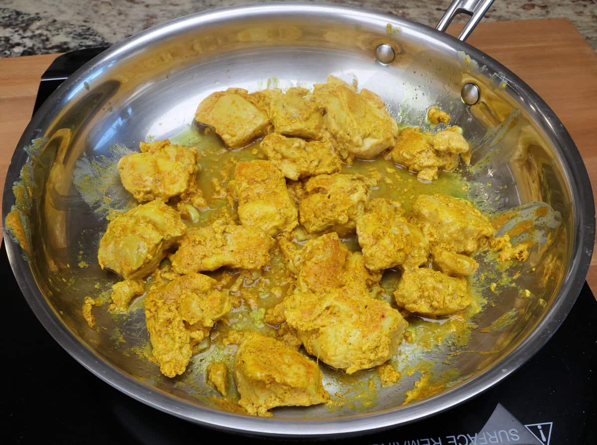 pieces of chicken that have been marinating in tikka masala sauce cooking in a skillet.