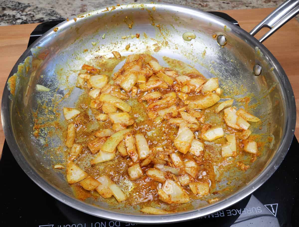 Indian spices cooking along with chopped onions in a skillet.