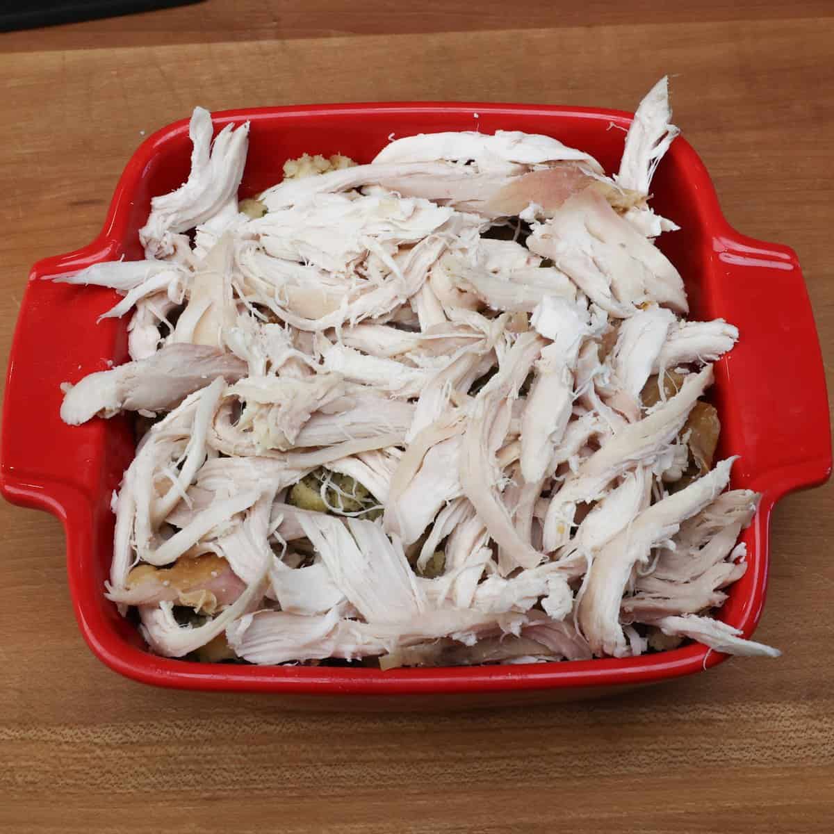 a layer of stuffing and a layer of leftover turkey on top of four bottom halves of Hawaiian rolls in a red baking dish.