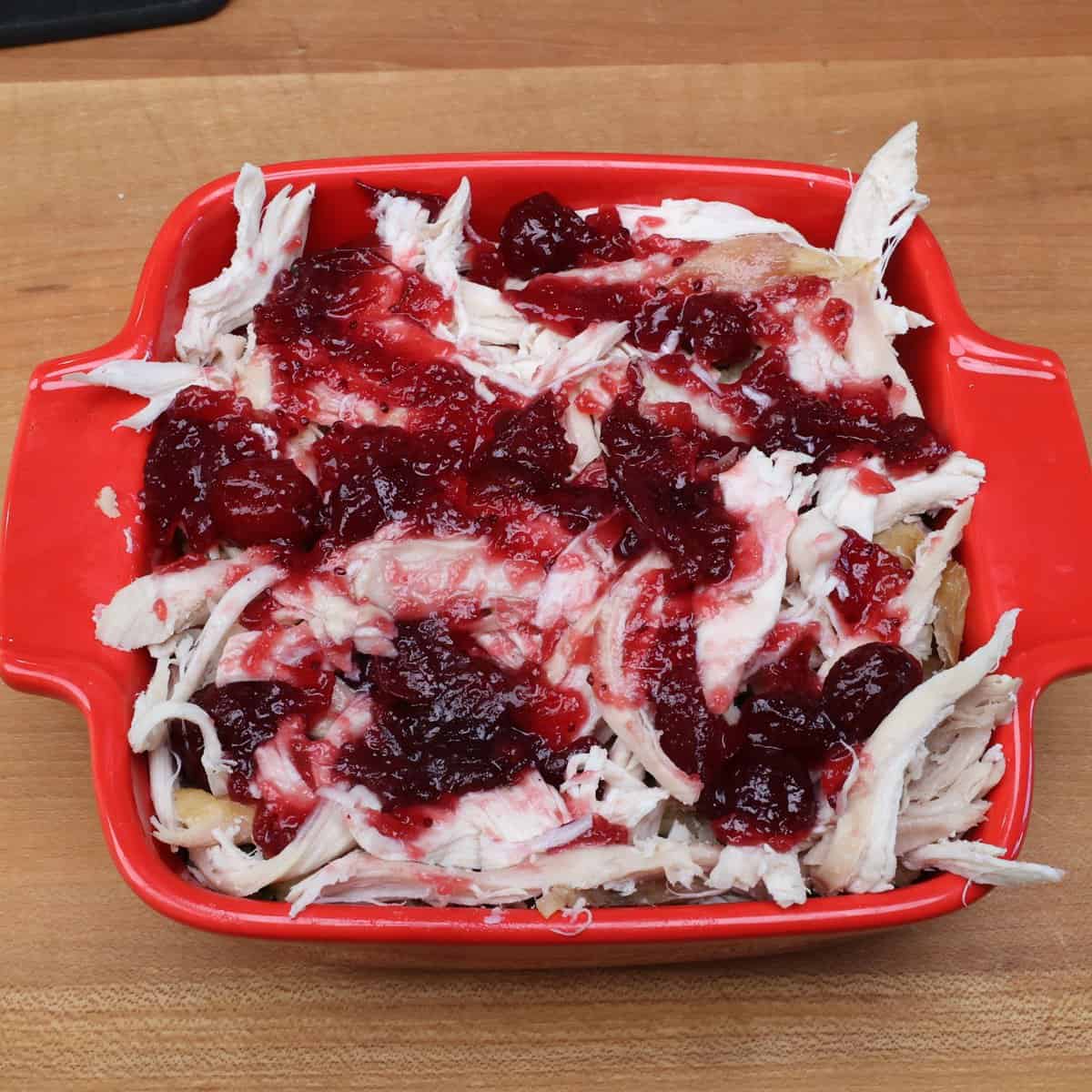 cranberry sauce on top of turkey over bread slices in a baking dish.
