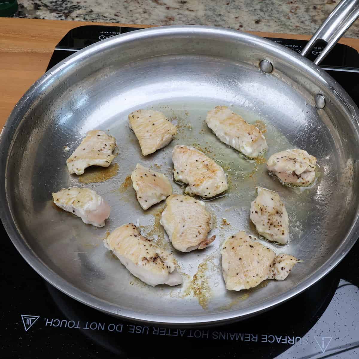 chicken pieces cooking in a skillet.