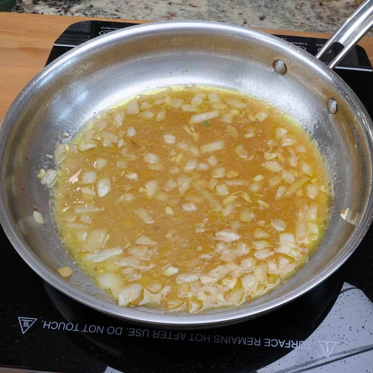 chicken broth, onions, and garlic simmering in a pan on the stove.
