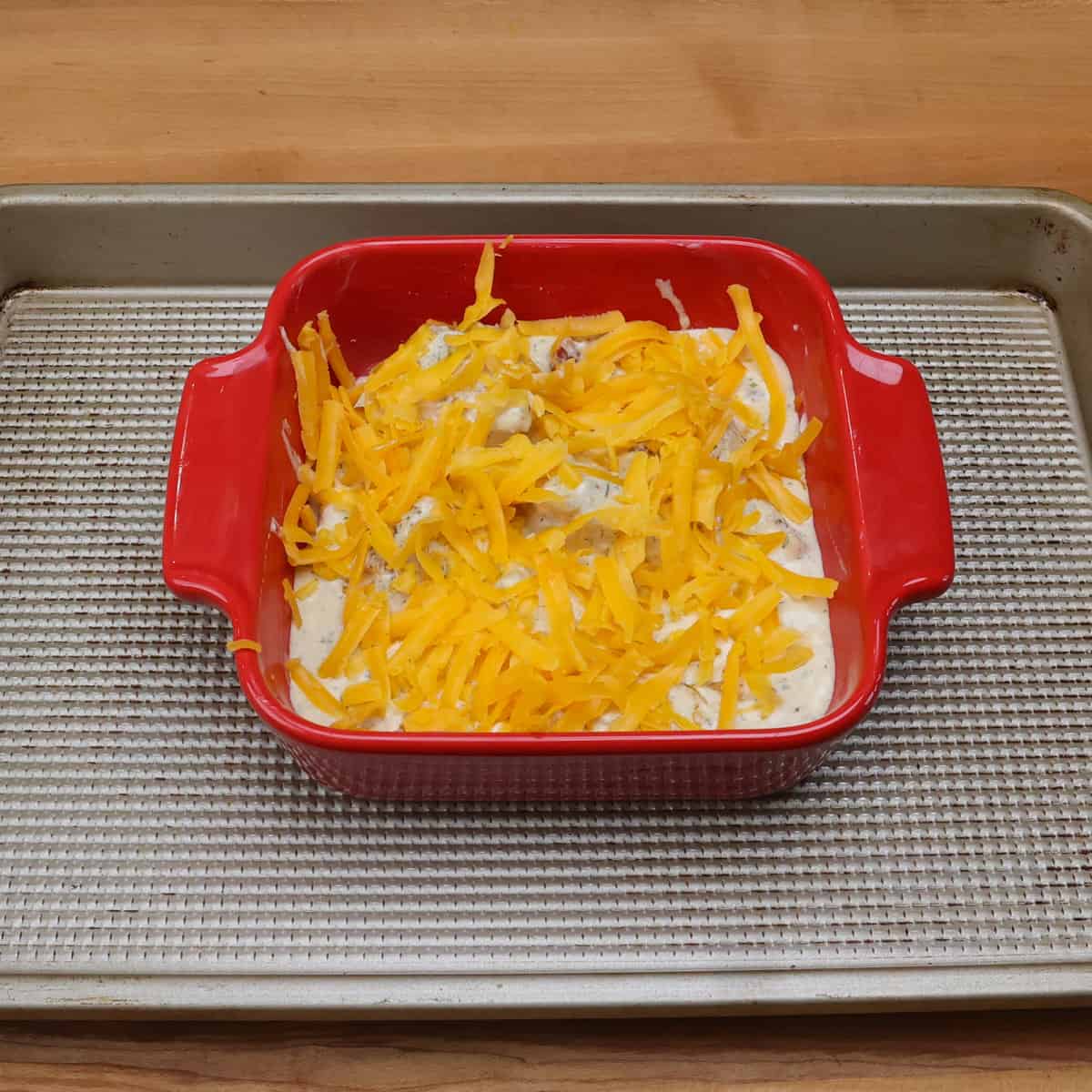 unbaked crack chicken topped with cheese on a rimmed baking sheet.