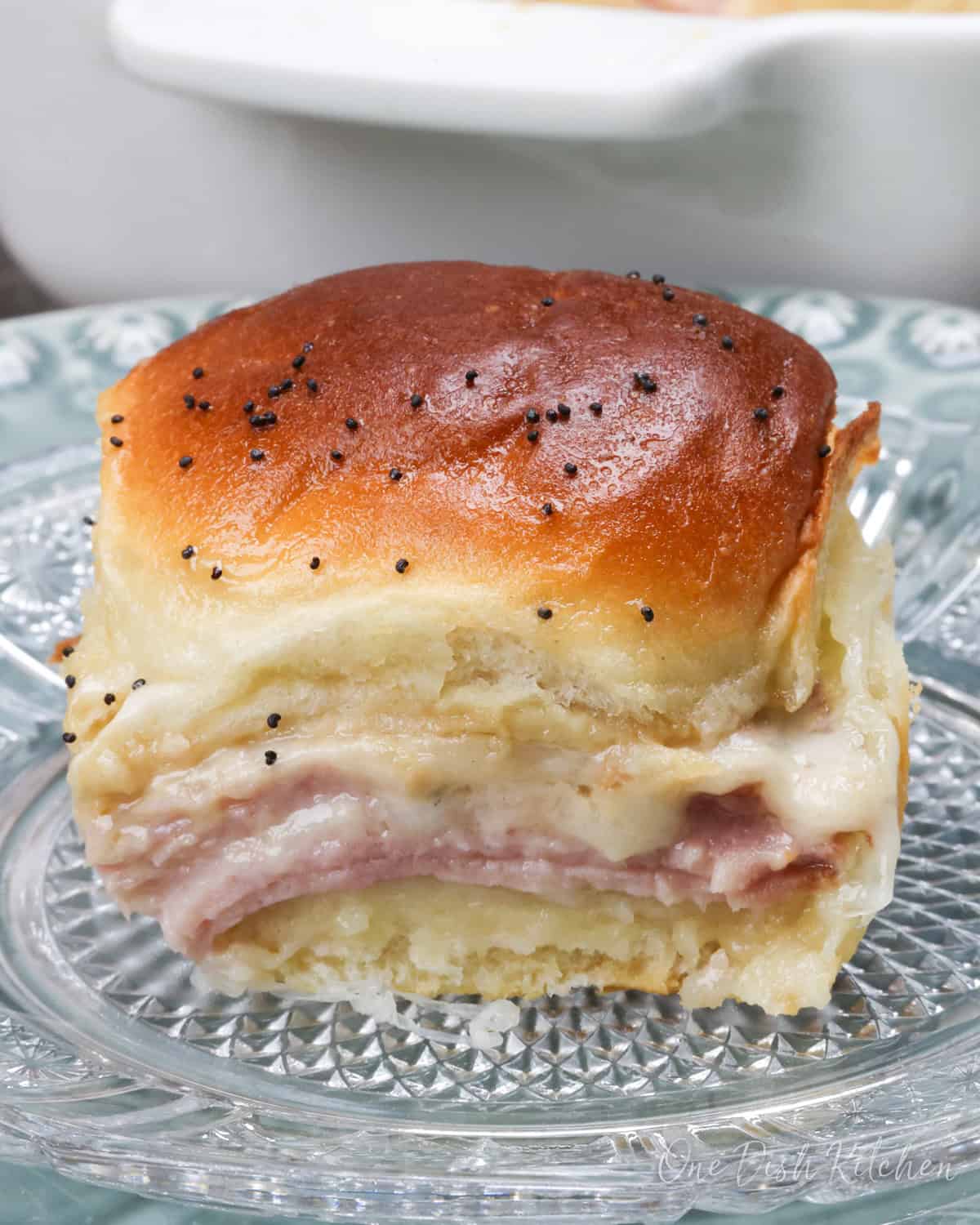 a hot ham and cheese slider next to a baking dish with a small batch of sliders.