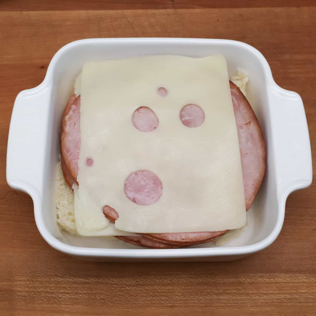 layering ham and cheese slices over the bottom half of Hawaiian rolls in a small baking dish.