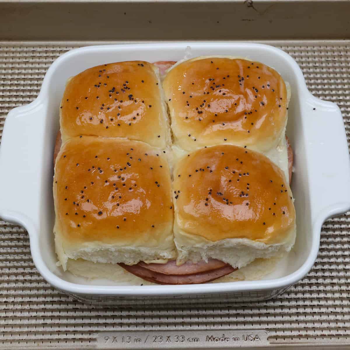 four unbaked ham and cheese sliders in a baking dish.