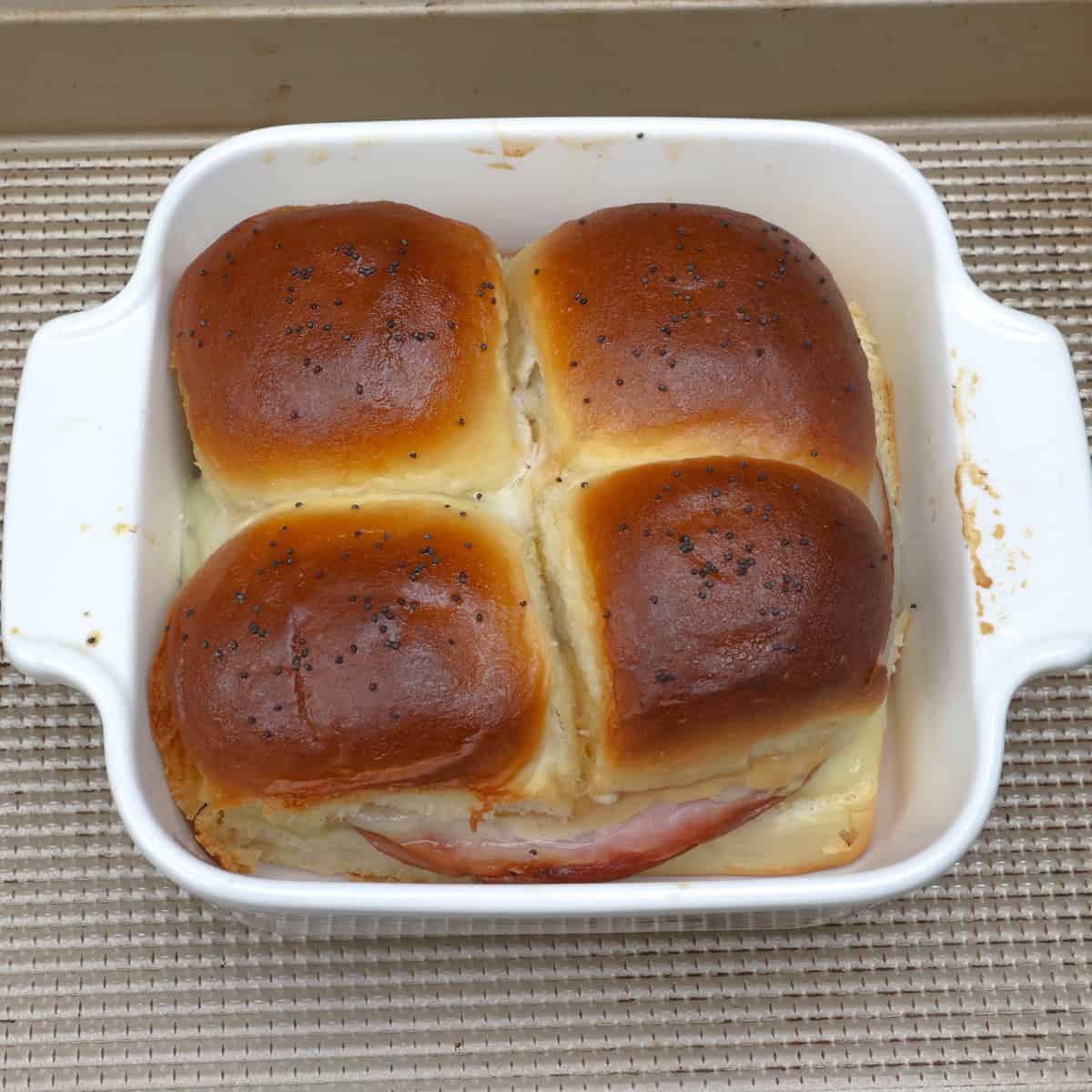 four baked ham and cheese sliders in a white baking dish.