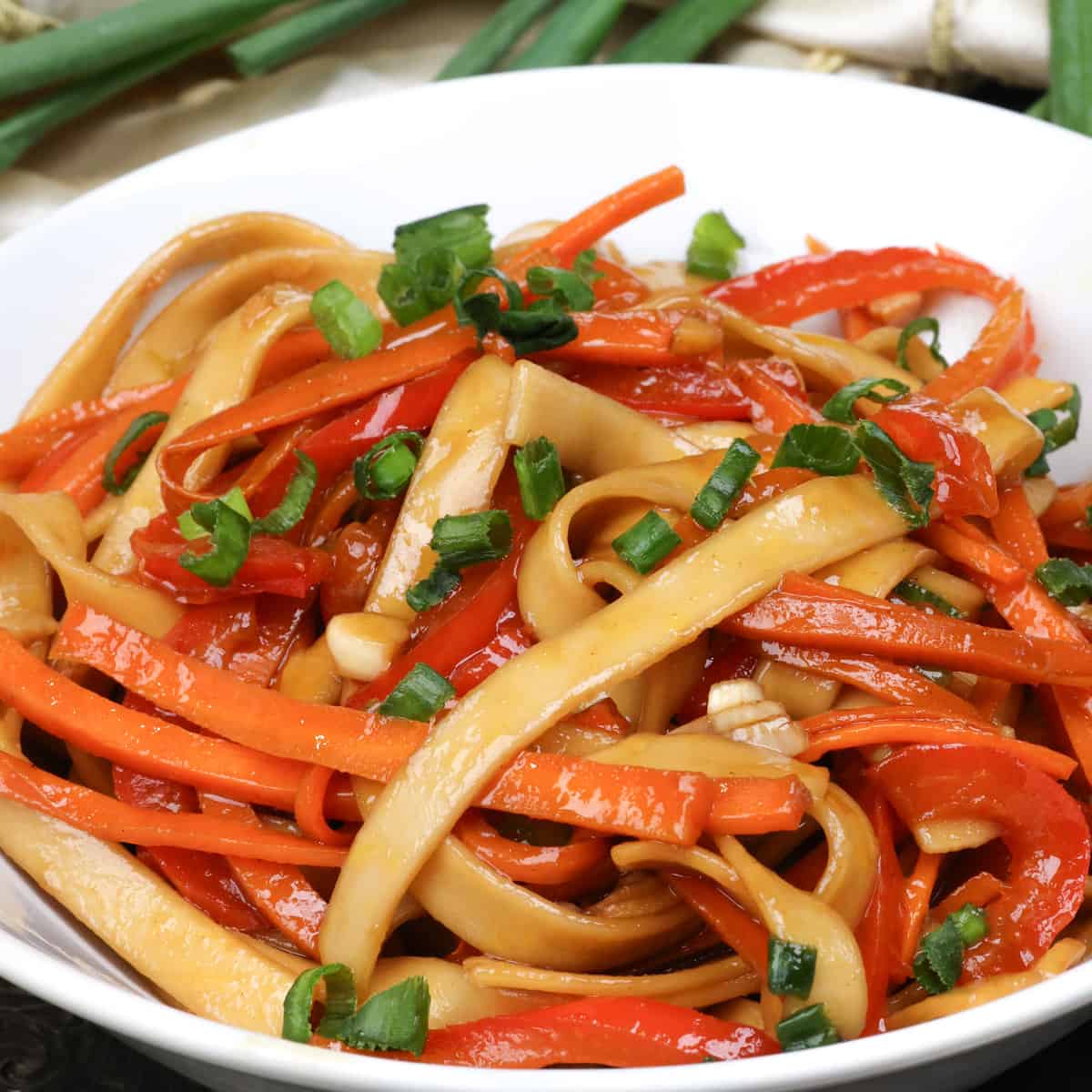 a white bowl filled with lo mein and topped with chopped green onions.