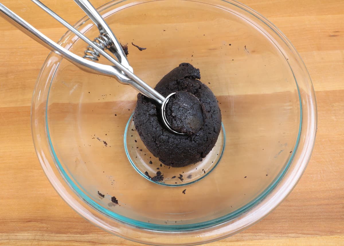 oreo cookie ball dough in a mixing bowl with a cookie scoop on top of the dough.