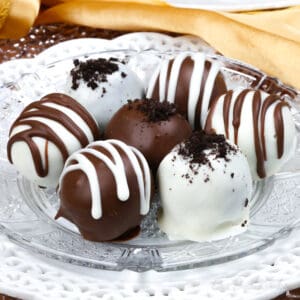 a plate of white and dark chocolate oreo balls next to a second plate of the chocolate dipped truffles and a gold napkin.