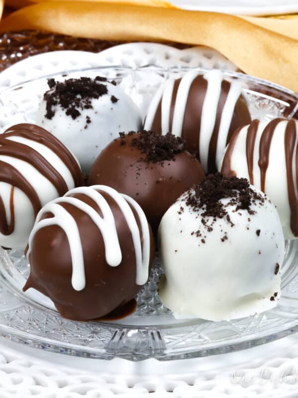 a plate of white and dark chocolate oreo balls next to a second plate of the chocolate dipped truffles and a gold napkin.
