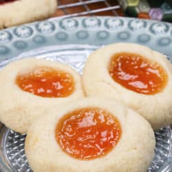 three thumbprint cookies filled with orange jam on a white plate.