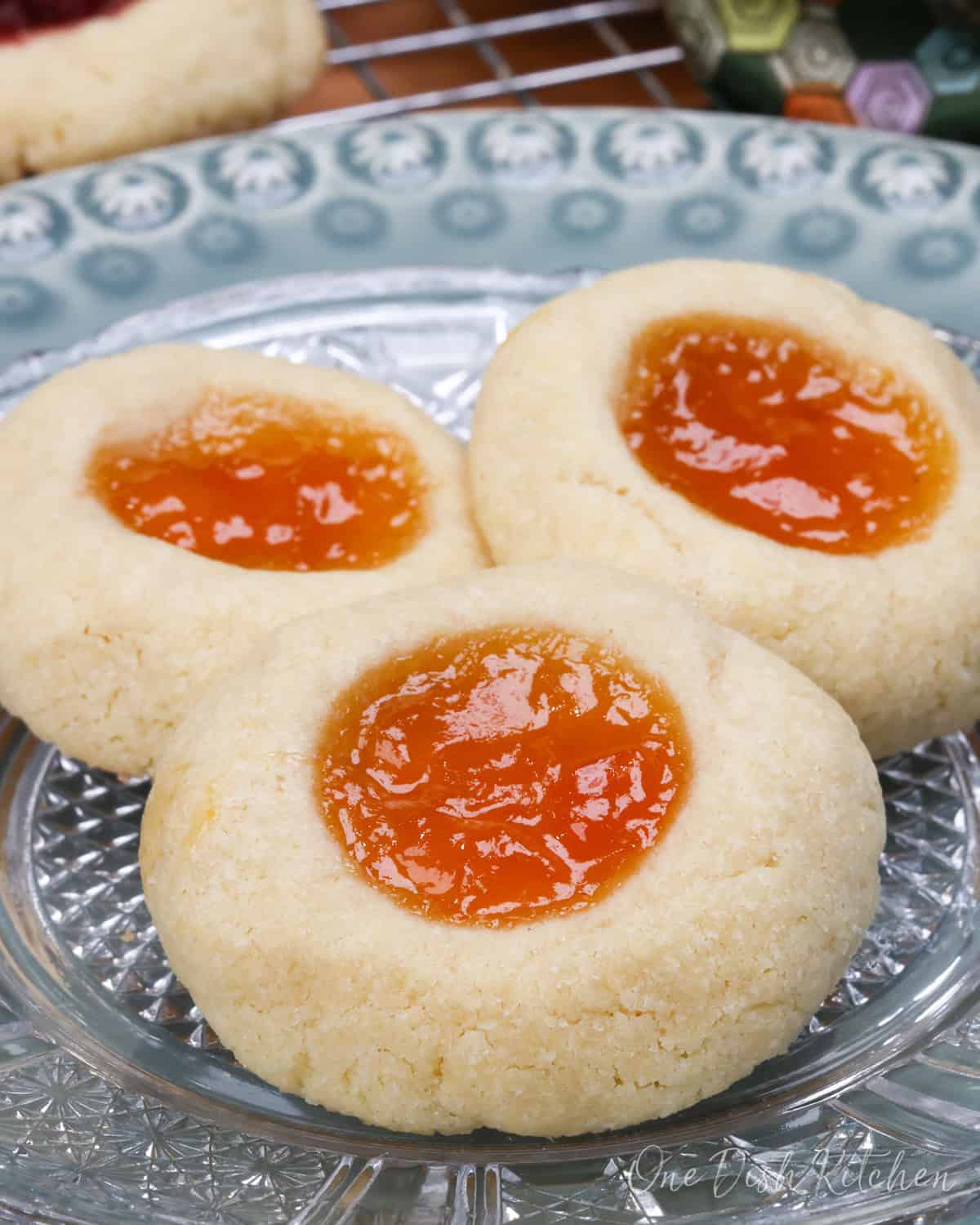 three thumbprint cookies filled with orange jam on a white plate.