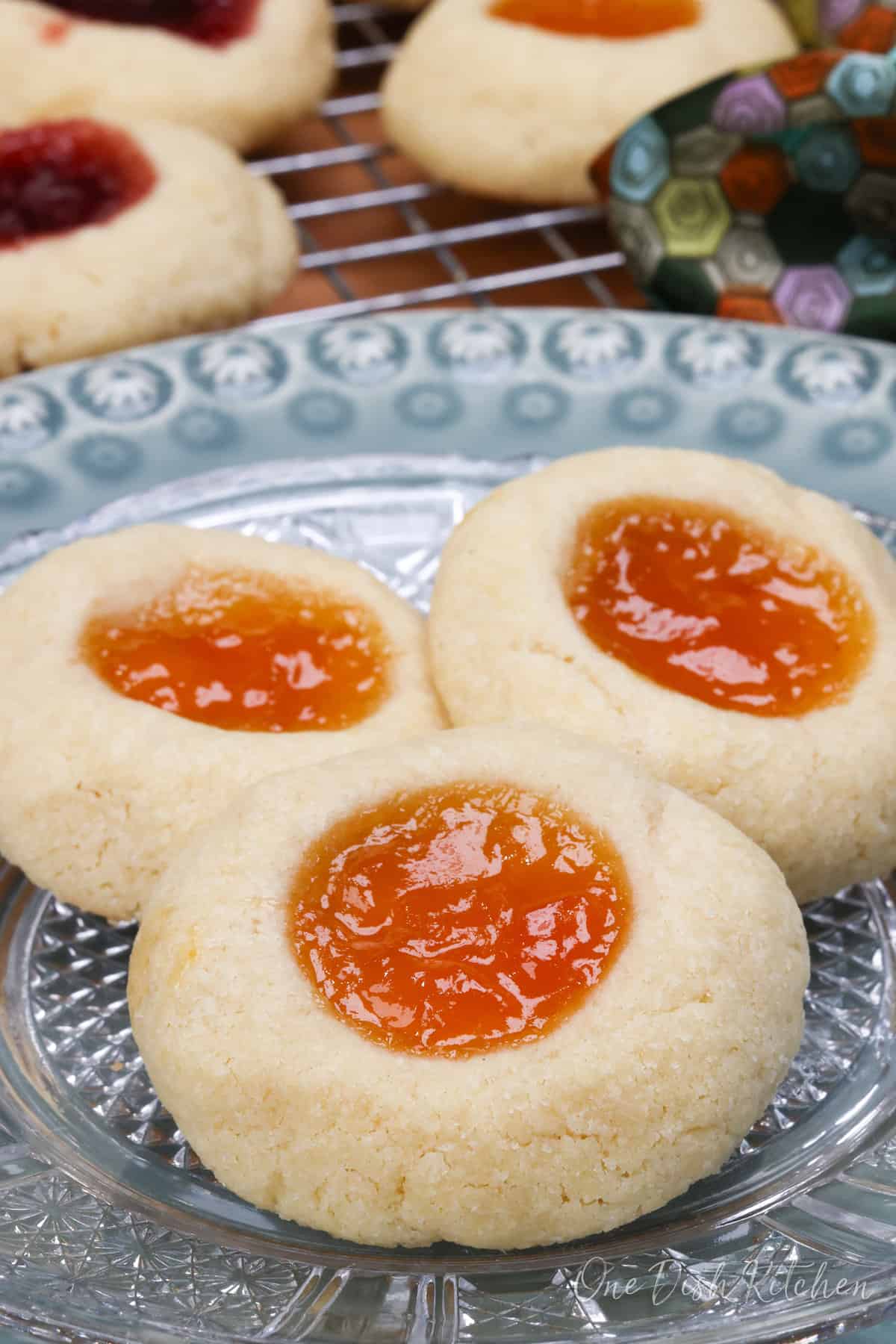 three thumbprint cookies filled with orange jam on a white plate.