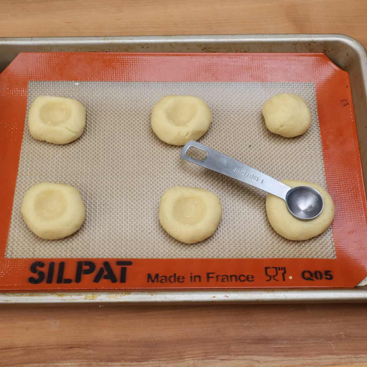 pressing a hole in the center of rolled cookie dough to form a thumbprint.